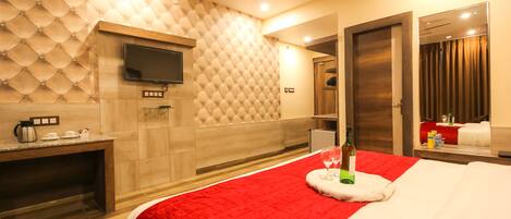 A modern hotel room with a large bed, a flat-screen TV mounted on the wall, a wooden desk, and a red accent wall.