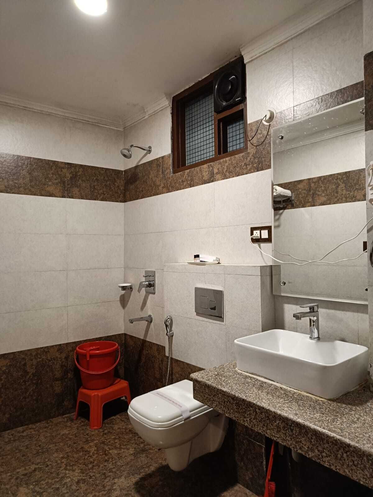 A bathroom with a toilet, sink, shower, and a red bucket.