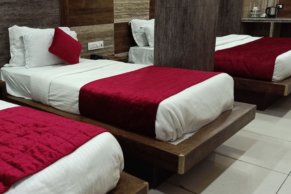 A hotel room with three beds, each with white bedding and red accents.
