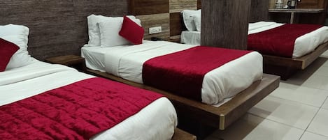A hotel room with three beds, each with white bedding and red accents.