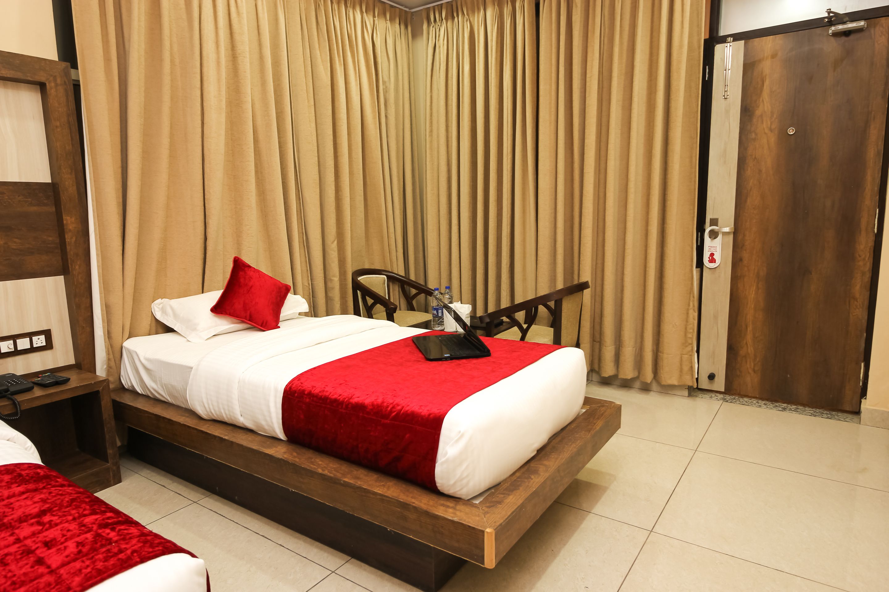 A hotel room with a wooden bed, a red and white bedspread, a bedside table with a phone, and a wooden wardrobe.