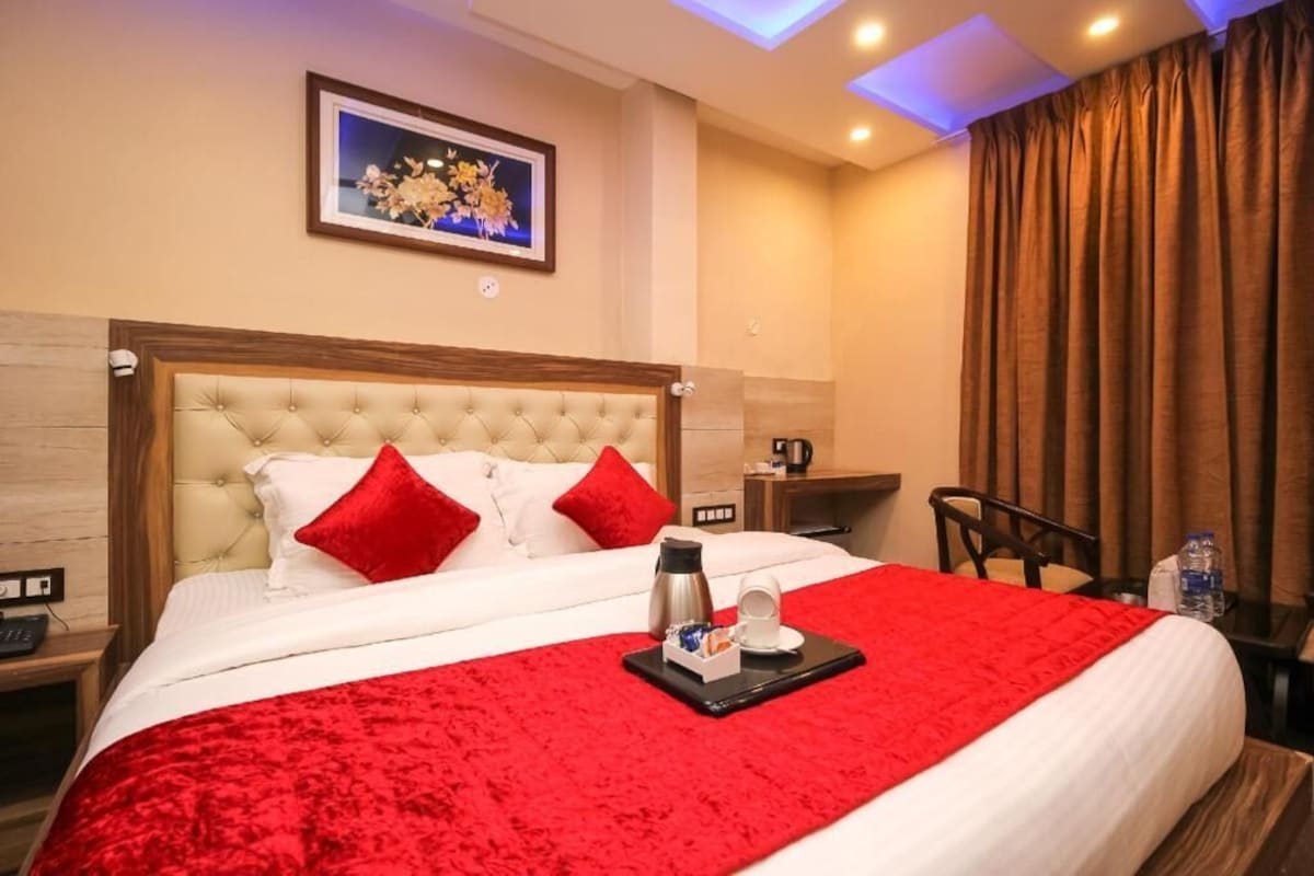 A hotel room with a large bed, red pillows, a coffee maker, and a framed picture on the wall.