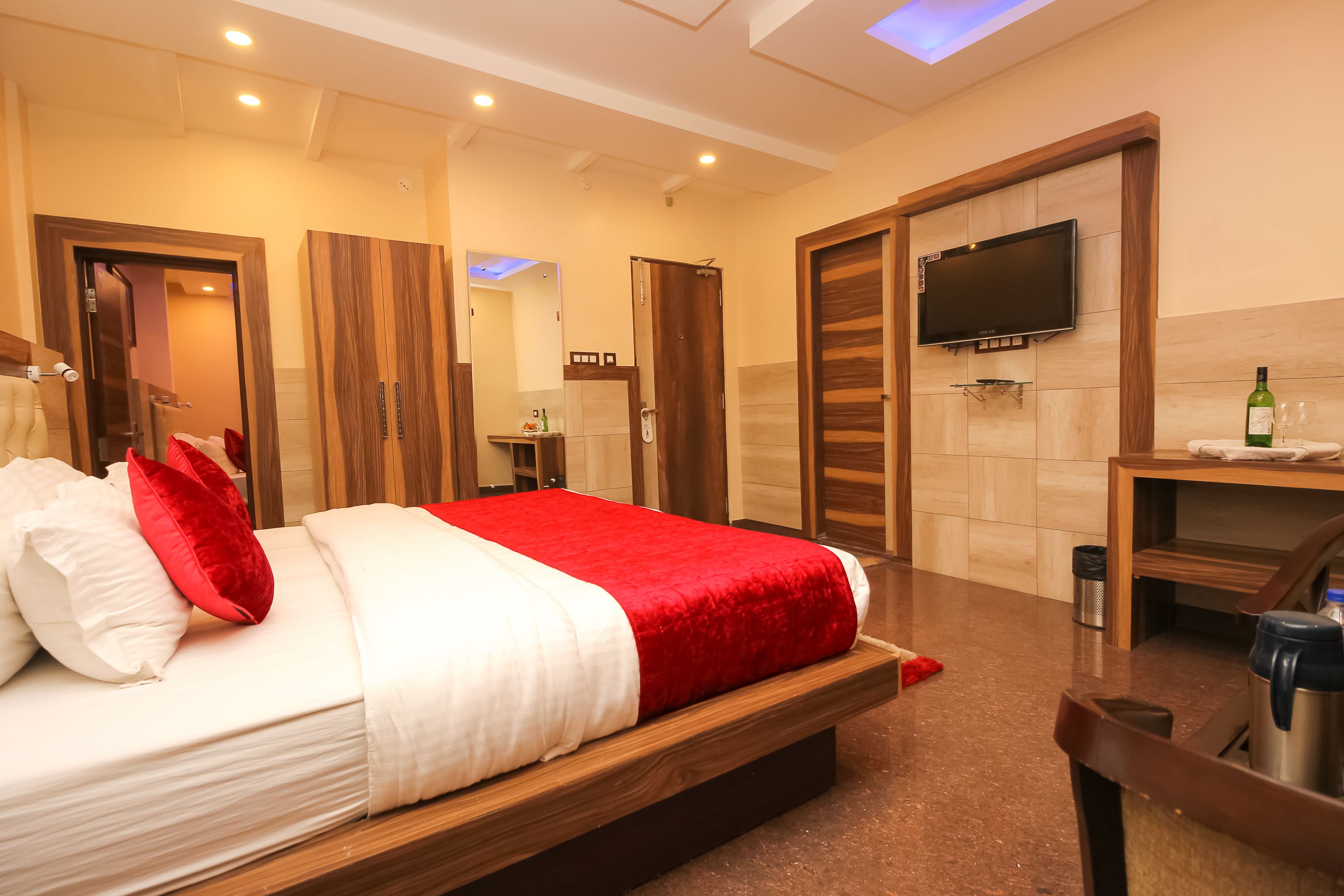 Une chambre d’hôtel moderne avec un grand lit, une armoire en bois, un téléviseur fixé au mur et un petit bureau avec une bouteille et un verre.