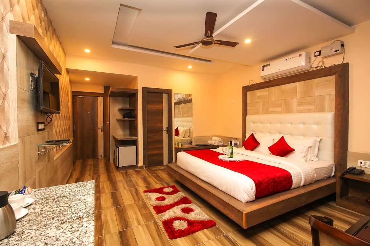 A hotel room with a bed, a TV, a ceiling fan, and a minibar.