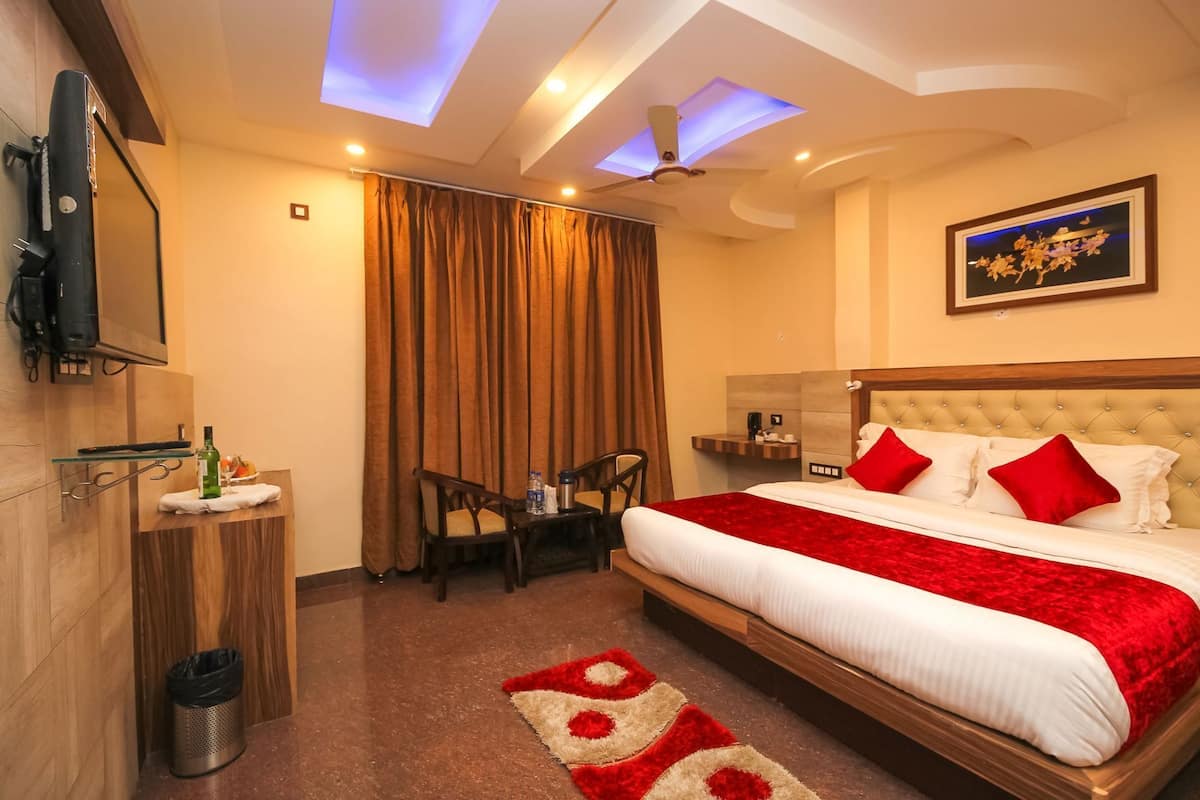 A hotel room with a bed, a desk, a chair, a TV, a ceiling fan, and a painting on the wall.