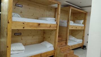 Tweepersoonsbed met houten frames en witte beddengoed, een kleine trap en een metalen prullenbak.
