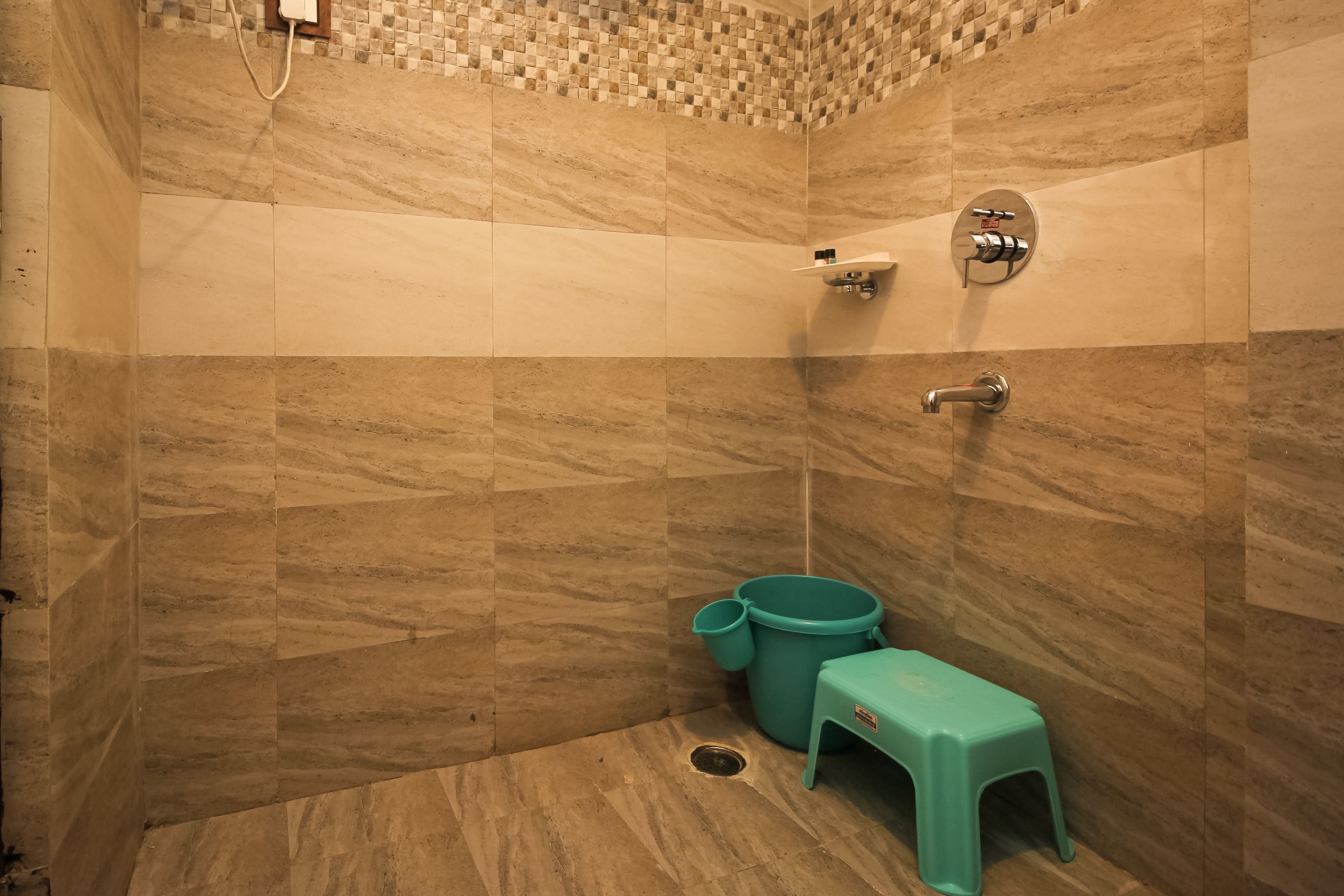 Ein Badezimmer mit gefliesten Duschwänden, einer Toilette und einem kleinen Hocker.