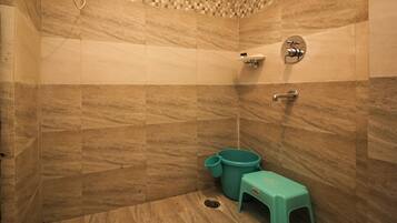 Un baño con pared de ducha enlosetada, un inodoro y un taburete pequeño.