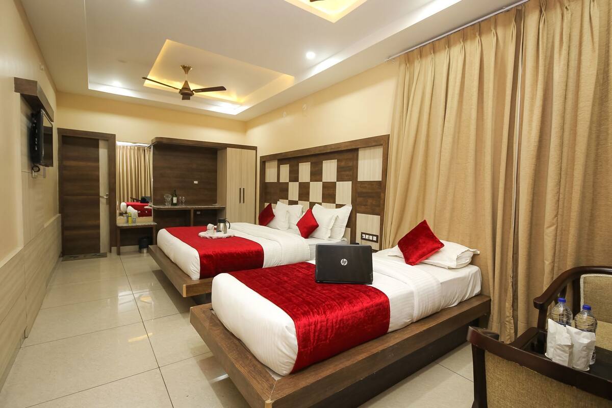 A hotel room with two beds, a laptop on one bed, a desk with a chair, and a mirror.