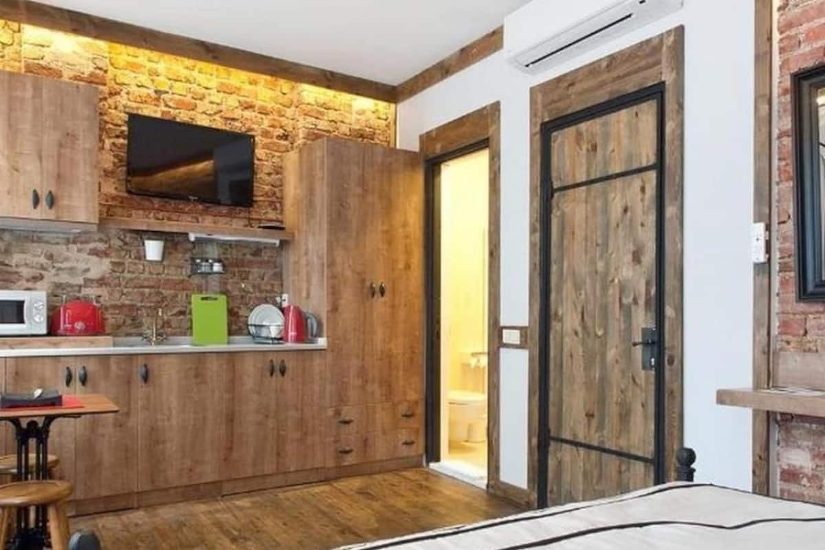 A compact kitchen with wooden cabinets, a microwave, and a television mounted on a brick wall.