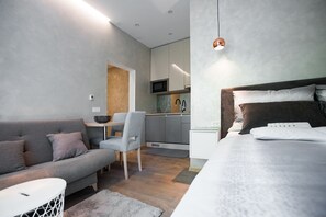 A modern bedroom with a large bed, a grey sofa, and a small dining area with a table and chairs.
