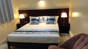 A neatly made bed with patterned bedding, two bedside lamps, a dark headboard, and a brown armchair. - Résidence De L'Amitié (Dakar)