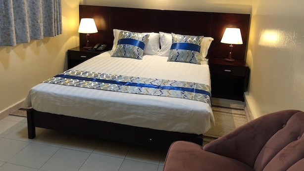 A neatly made bed with a patterned bedspread, two bedside lamps, and a nightstand with a phone. - Résidence De L'Amitié (Dakar)