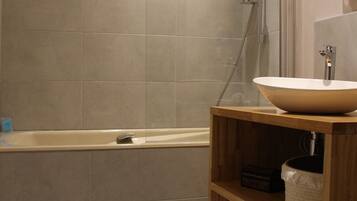 A bathroom with a bathtub, a wooden vanity with a sink, and a shower area.