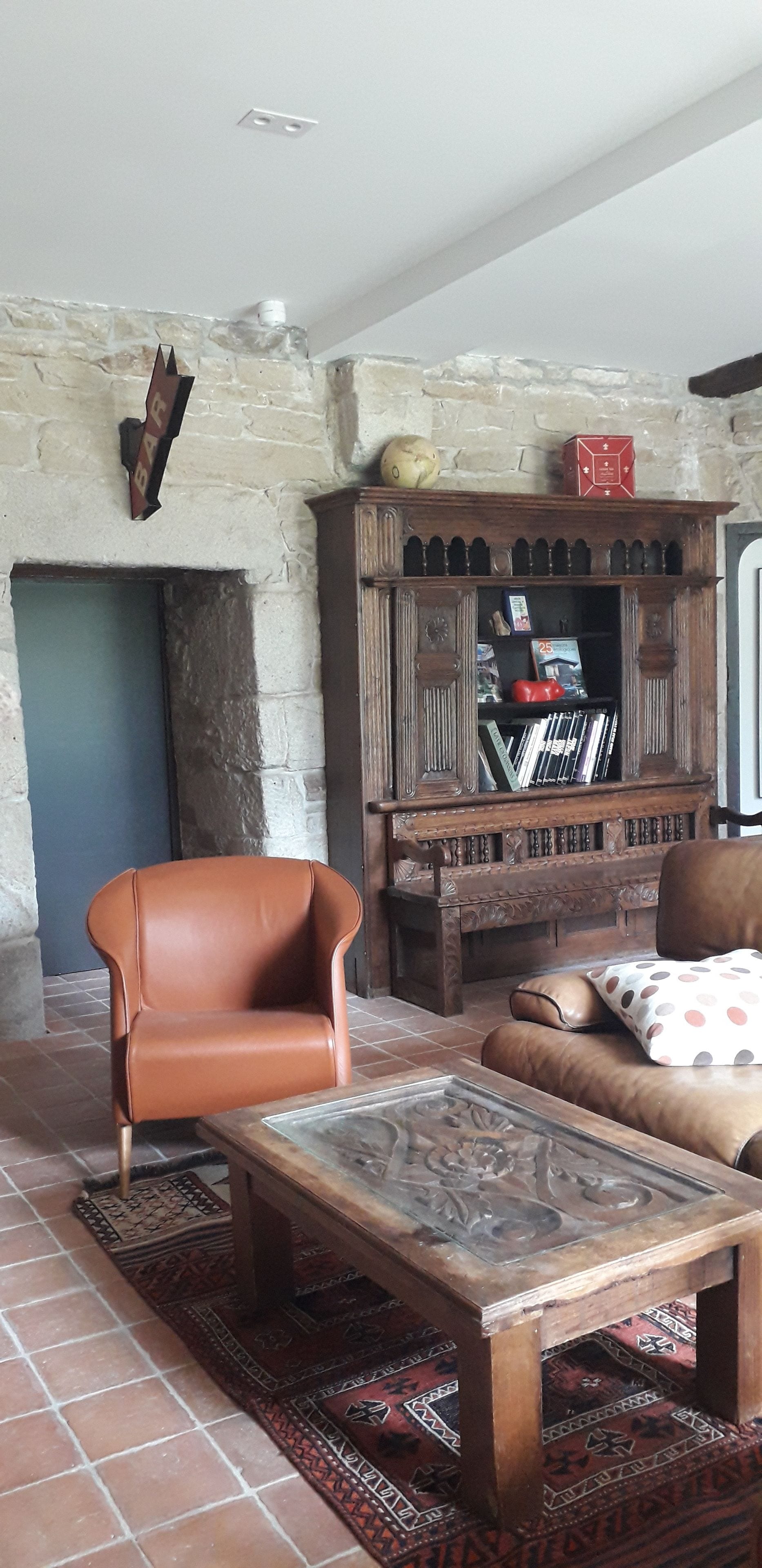 A living room with a stone wall, a fireplace, a wooden cabinet with books, a leather armchair, and a coffee table.