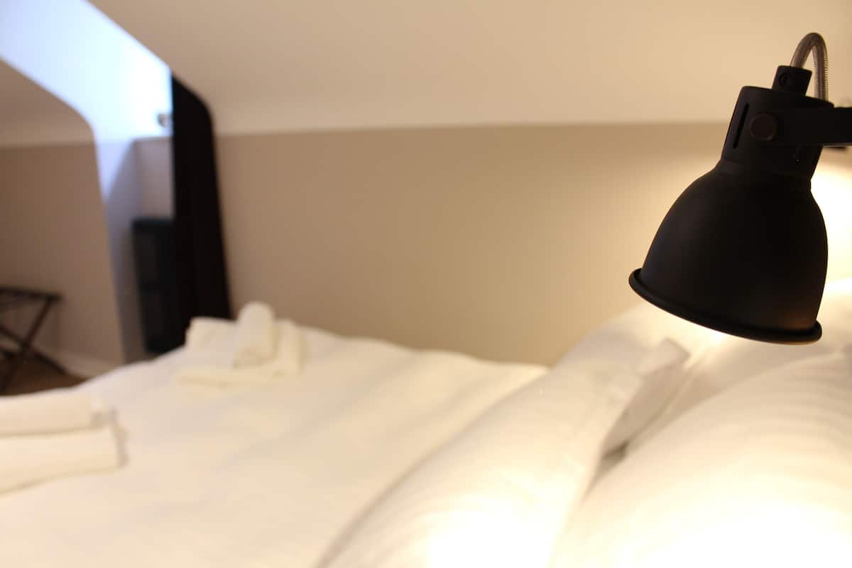 Una cama bien tendida con sábanas blancas y una lámpara negra a la derecha.