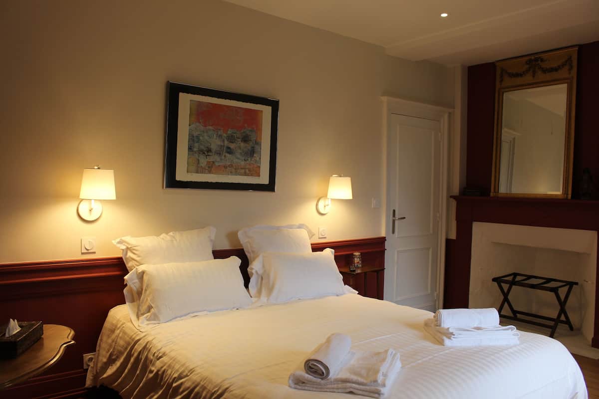 Habitación de hotel con una cama bien hecha, dos lámparas de noche, una obra de arte enmarcada en la pared y una chimenea.