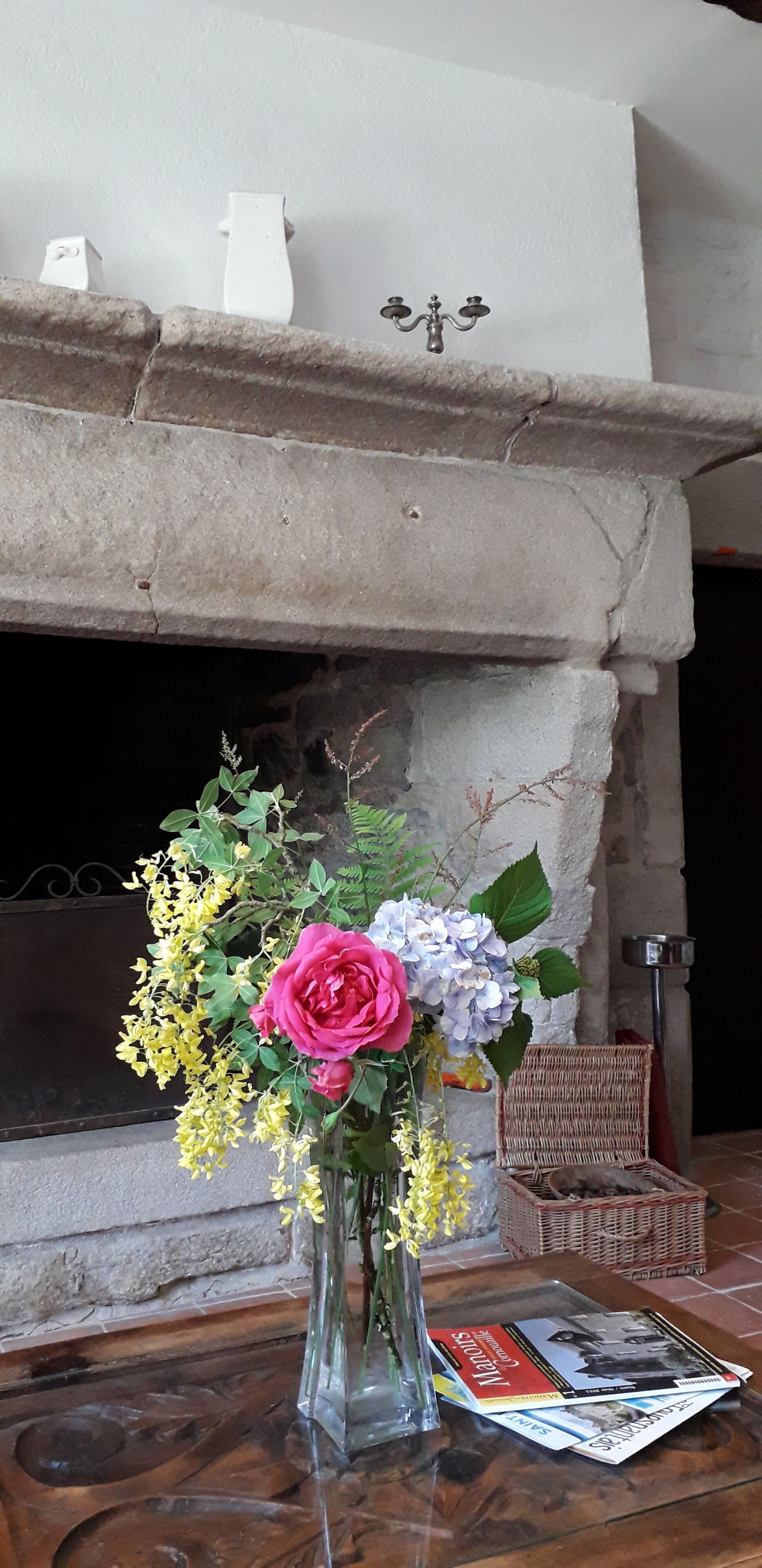 A vase with flowers on a wooden table in front of a fireplace.