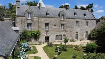 Un bâtiment en pierre doté d’une entrée centrale, de nombreuses fenêtres et d’un jardin aménagé avec des espaces pour s’asseoir à l’extérieur.