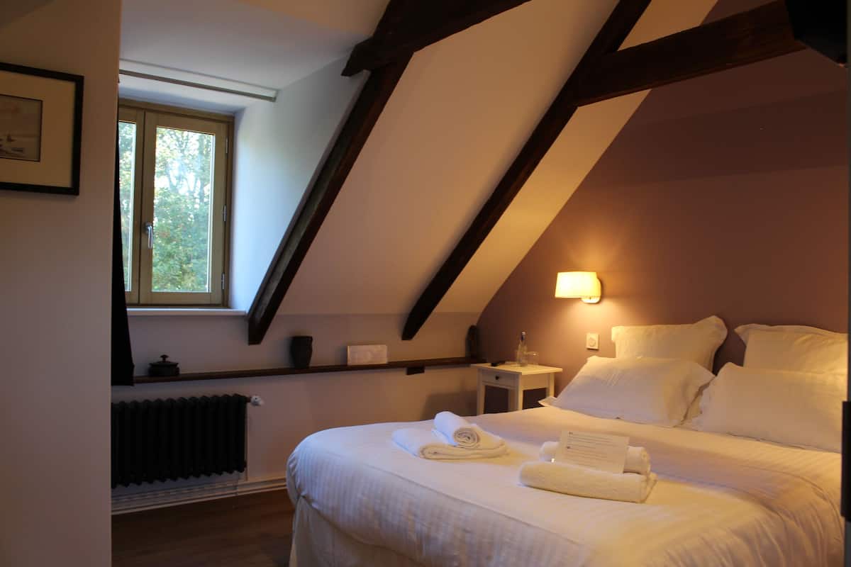 Un dormitorio con techo inclinado, una ventana, una mesita de noche y una cama con almohadas y toallas.