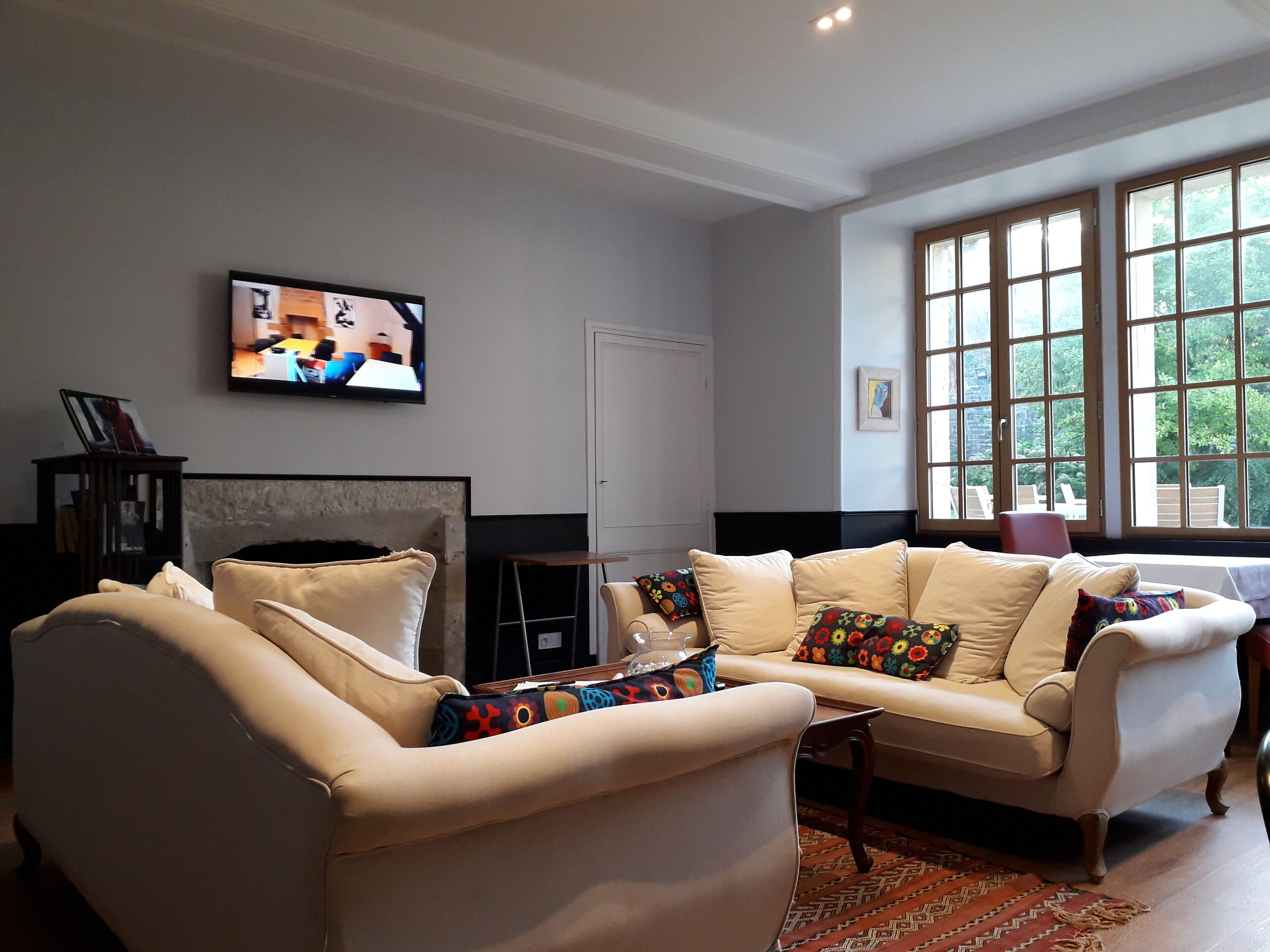 Una sala de estar con un sofá color beige, un televisor montado en la pared y un ventanal con vistas al verdor exterior.
