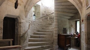 Una escalera de piedra con barandilla de madera, una puerta de madera al final e igualmente un farol en la pared.