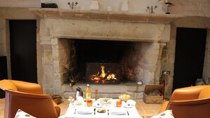 Un comedor con chimenea de piedra, sillas de cuero, una mesa dispuesta para dos personas y una cesta de pan.