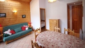 Ett mysigt rum med ett träpanelat tak, en grön soffa, ett matbord med en mönstrad duk och ett träskåp.