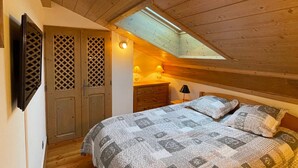 A bedroom with a sloped ceiling, a bed with a patterned quilt, a bedside lamp, and a wooden wardrobe.