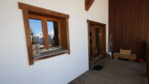 A wooden deck with a wooden bench and a door leading to a room.