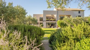 Une maison moderne à deux étages, avec un chemin pavé menant à l’entrée, entourée d’une végétation luxuriante et d’arbres.