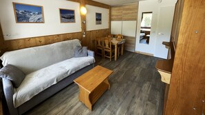 A cozy room with a wooden ceiling, a sofa, a wooden table, and a dining area with chairs. - Renovated ski-in studio, 4 people, Les Menuires (Les Menuires)
