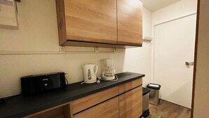 A small kitchenette with wooden cabinets, a black countertop, a coffee maker, and a trash bin. - Renovated ski-in studio, 4 people, Les Menuires (Les Menuires)
