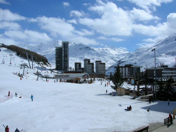 A snow-covered ski resort with buildings, a ski lift, and a mountainous backdrop.