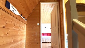 A wooden hallway leading to a bedroom with a bed, a door, and a wall-mounted sign. - Charming Breton House Steps from Saint-Guirec Beach, Ploumanac’h – 2 Beds, Garden, Pet-Friendly (Perros-Guirec)