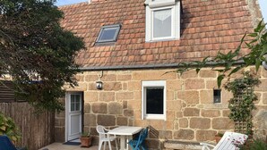 A stone house with a tiled patio, a small table and chairs, and a wooden fence. - Charming Breton House Steps from Saint-Guirec Beach, Ploumanac’h – 2 Beds, Garden, Pet-Friendly (Perros-Guirec)