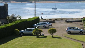A parking area with cars, a grassy foreground, and a view of a body of water with a boat in the distance. - Renovated apartment with terrace 200m from beaches in Trégastel (Trégastel)