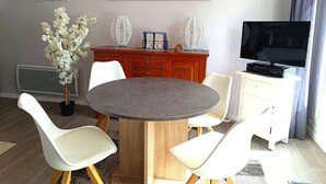 A modern living room with a round dining table, white chairs, a TV, and decorative items. - Renovated apartment with terrace 200m from beaches in Trégastel (Trégastel)