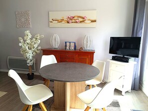 Una sala moderna con una mesa de comedor redonda, sillas blancas, un televisor y objetos decorativos.