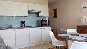 A compact kitchen with white cabinets, a microwave, a coffee maker, and a dining area with a round table and chairs. - Renovated apartment with terrace 200m from beaches in Trégastel (Trégastel)