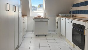 Una cocina compacta con ventana, lavadora, lavavajillas y horno empotrado.