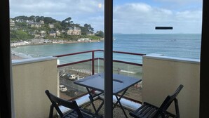 Un balcón con mesa y sillas con vistas a un pueblo costero, edificios y una playa.