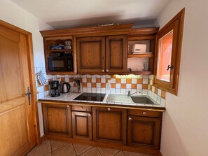 A compact kitchen with wooden cabinets, a microwave, a coffee maker, and a sink.