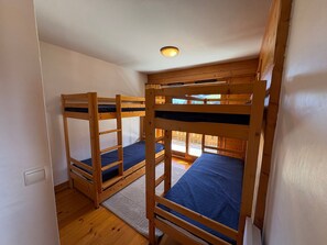 A room with bunk beds, wooden flooring, a white wall, and a ceiling light.