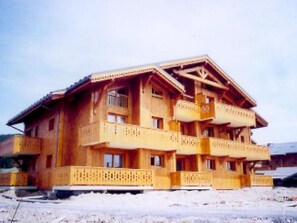 Een meerhoog gebouw van hout, met balkons en een schuin dak, waarschijnlijk een hotel of verblijfsoord.