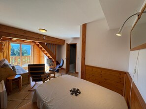 Een slaapkamer met een bed, een stoel, een klein tafeltje, een trap en uitzicht op het landschap.