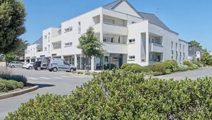 Un hotel moderno de varios pisos con techo plano, ventanas amplias y un estacionamiento frente a él.
