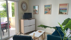 Una sala de estar con sofá, televisor en un mueble, una mesa con planta y un balcón con mesa y sillas.