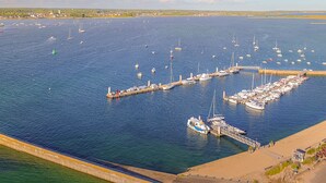 Un puerto deportivo con numerosas embarcaciones amarradas, un muelle que se adentra en el agua y una zona de playa arenosa.