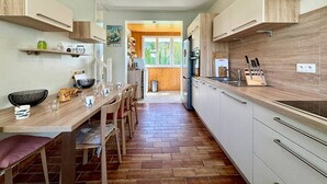 Et moderne køkken med træskabe, klinkegulv i mursten og et spiseområde med bænk og stole.